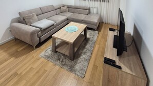 Un salon comprenant un canapé d’angle, une table basse, un téléviseur et une télécommande posée sur un support en bois.