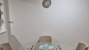 Une table ronde en verre, quatre chaises, une horloge au mur et un petit bol décoratif posé sur la table.