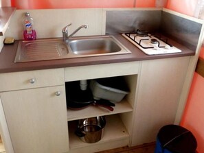 Una cocina compacta con fregadero, grifo y estufa a gas.