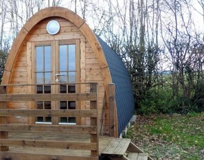 A wooden cabin with a pitched roof, a front door with glass panels, and a small wooden deck.
