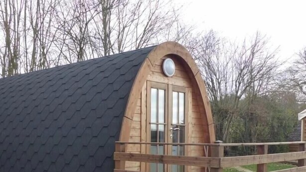 A wooden cabin with a sloped roof, a wooden deck, and a single door.