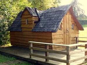 A wooden cabin with a sloped roof, a chimney, and a wooden deck leading to the entrance.