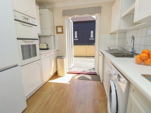 A kitchen with a washing machine, a trash bin, and a sink with oranges. - Anchorage House (Seaview)