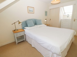 A bedroom with a bed, two bedside tables with lamps, a dresser, a door, and a window. - Anchorage House (Seaview)