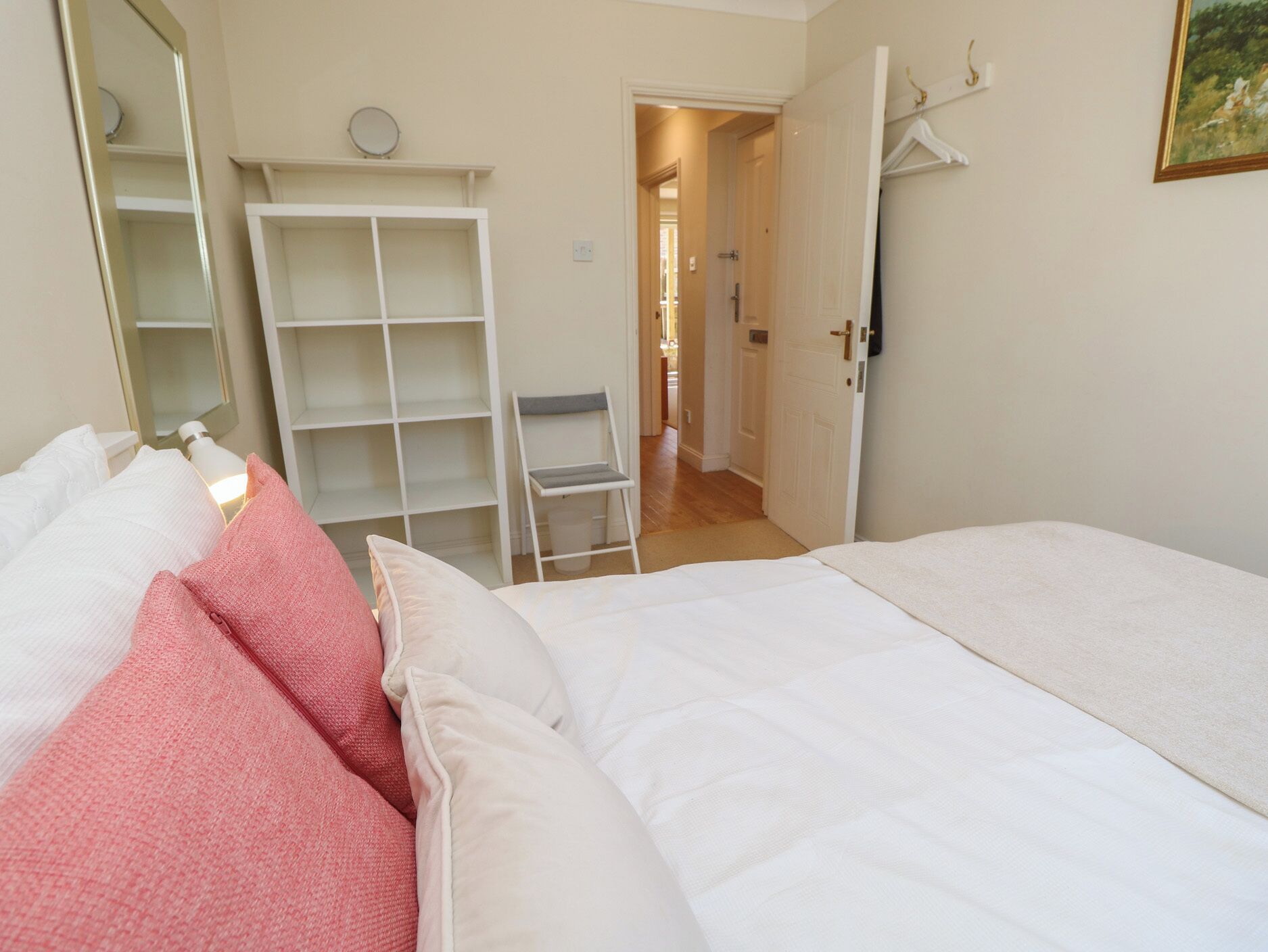 A bedroom with a bed, a wardrobe, a mirror, and a door leading to another room.