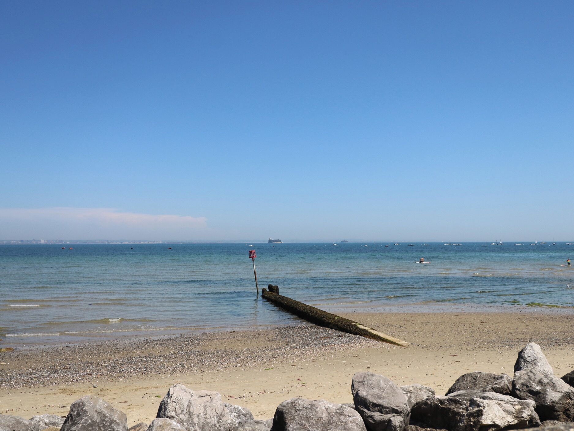 A beach with a wooden structure extending into the water, pebbles, and rocks in the foreground.