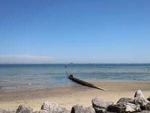A beach with a wooden structure extending into the water, pebbles, and rocks in the foreground. - Anchorage House (Seaview)