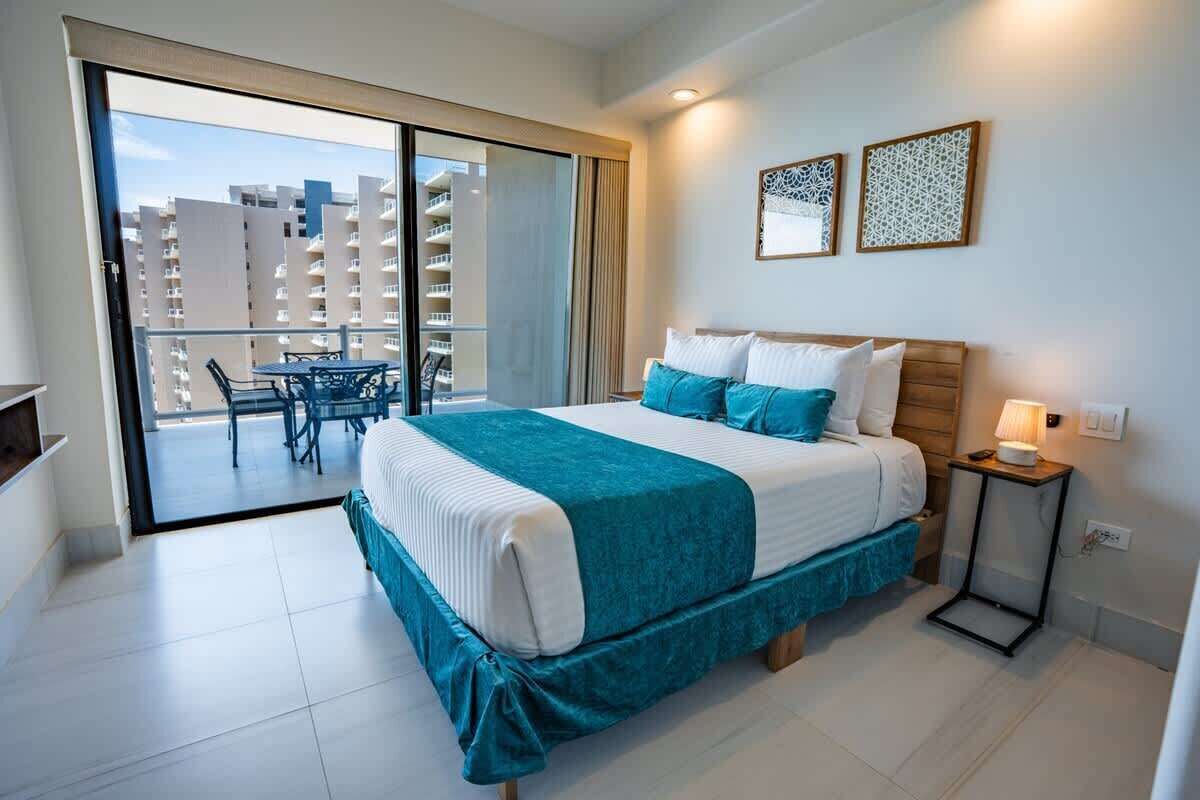 Ein Hotelzimmer mit Bett, Nachttisch, Lampe und Blick ins Freie.