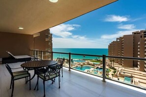 A balcony with a table and chairs, overlooking a pool area and ocean. - Topaz 701 |Oceanfront Luxury Condo at Las Palomas (Puerto Peñasco)