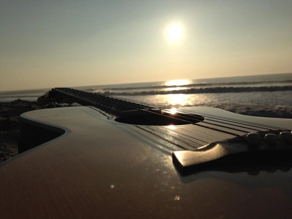 En gitarr på en strand med en solnedgång i bakgrunden.