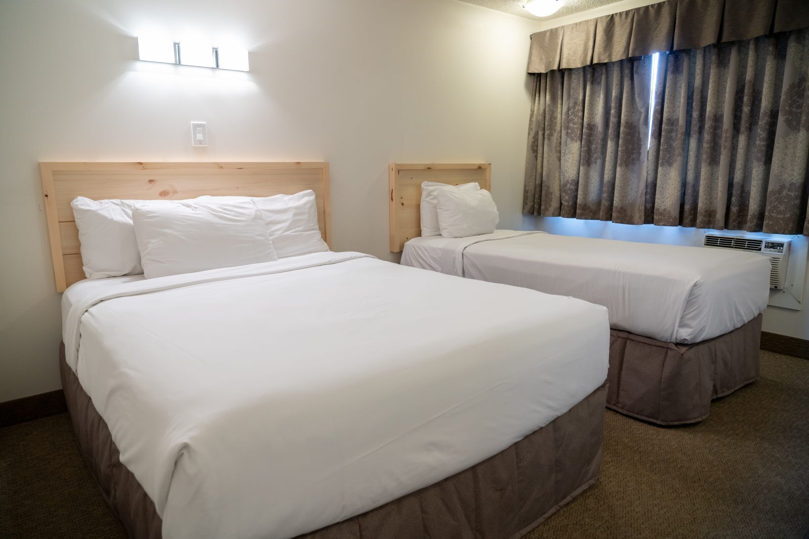 Quarto de hotel com duas camas, janela com cortinas, ar condicionado fixado na parede e luz no teto.