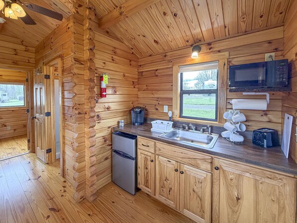 A wooden cabin kitchen with a refrigerator, sink, microwave, and coffee maker.