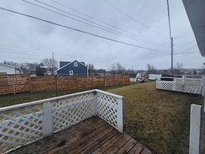 A backyard with a wooden deck, a white fence, and a blue house in the background.