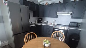 Una cocina moderna con armarios oscuros, electrodomésticos de acero inoxidable y una mesa de comedor de madera con sillas.