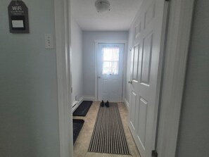A hallway with a door, a doormat, a rug, and a WiFi password sign.
