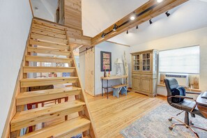Eine Holztretreppe führt zu einer erhöhten Ebene, ein Schreibtisch mit Stuhl, ein Schrank und ein Fenster mit Jalousien.