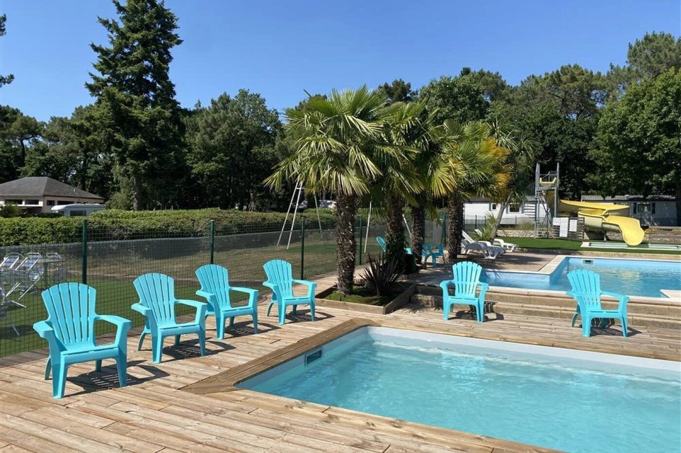 Een zwembadgedeelte met blauwe Adirondack-stoelen, een houten terras en een kleine glijbaan.