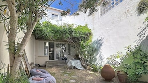Un patio con un edificio blanco, un árbol, un sillón informal y una planta en maceta.