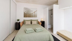 Un dormitorio con cama, mesita de noche y una obra de arte en la pared, además de una puerta abierta a un baño.