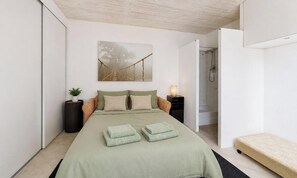 Ein Schlafzimmer mit einem Bett, einem Nachttisch, einem Wandbild und einer offenen Tür zu einem Badezimmer.