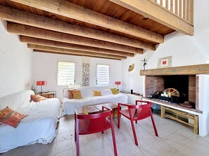 Ein Zimmer mit Holzboden, Kamin, einem Bett mit Kissen, einem Tisch mit Stühlen und Kunstwerken an den Wänden.