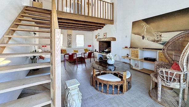Un amplio salón con una escalera de madera alta, una mesa redonda y muebles de mimbre.