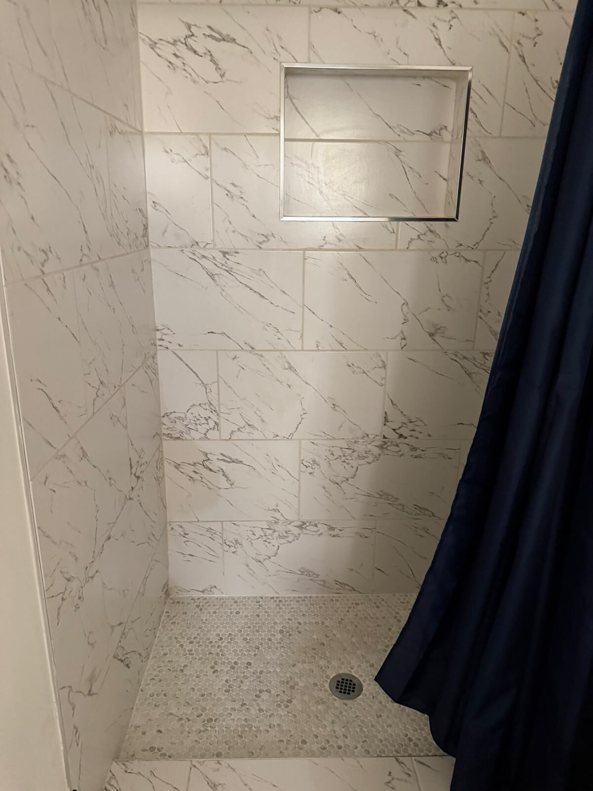 Une douche avec des carreaux de marbre et un drain.