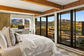 Ein Schlafzimmer mit einem großen Bett, einem Schreibtisch und Blick auf eine gebirgige Landschaft durch große Fenster.