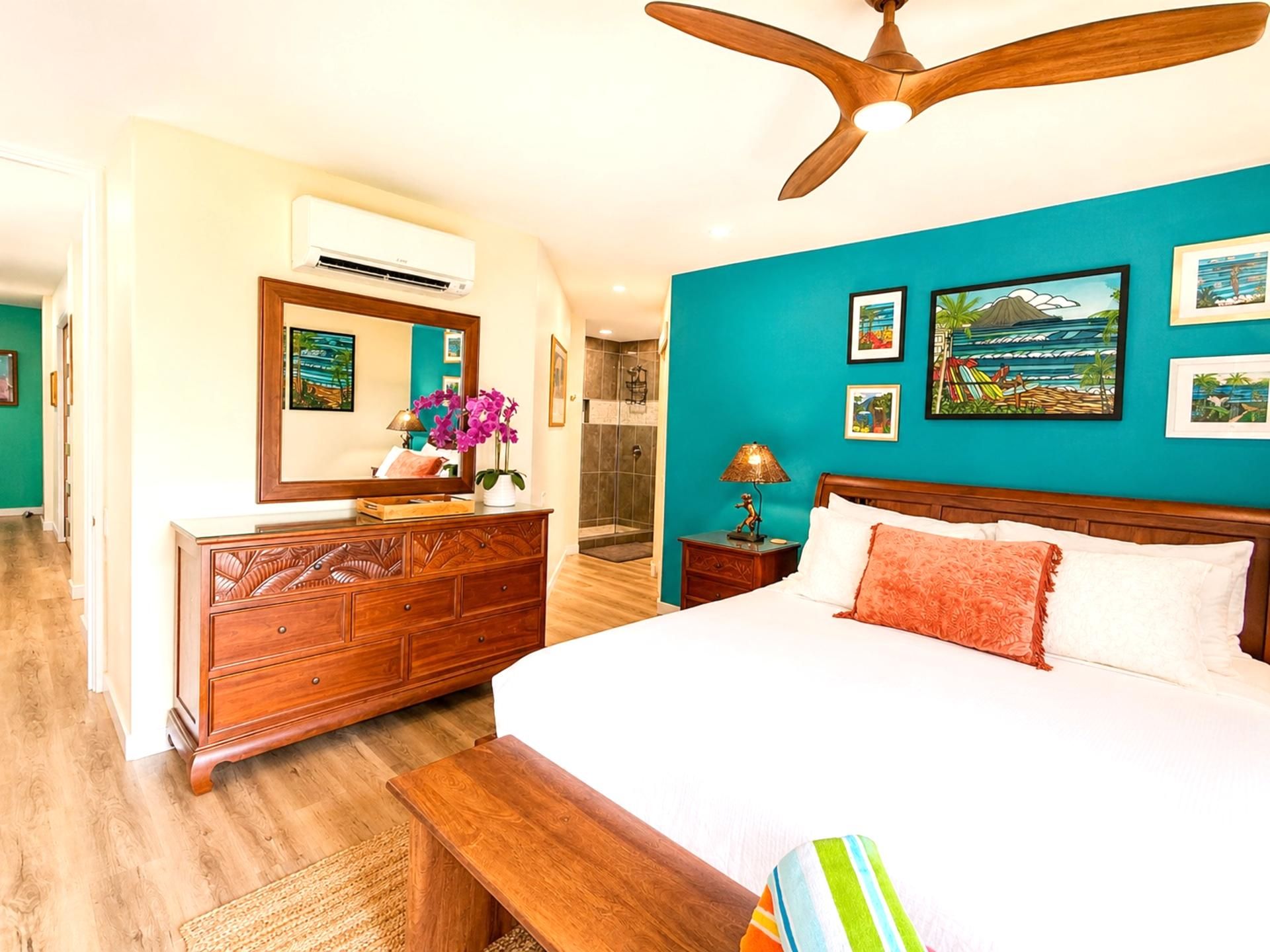 A bedroom with a bed, wooden dresser, ceiling fan, and artwork on teal walls.