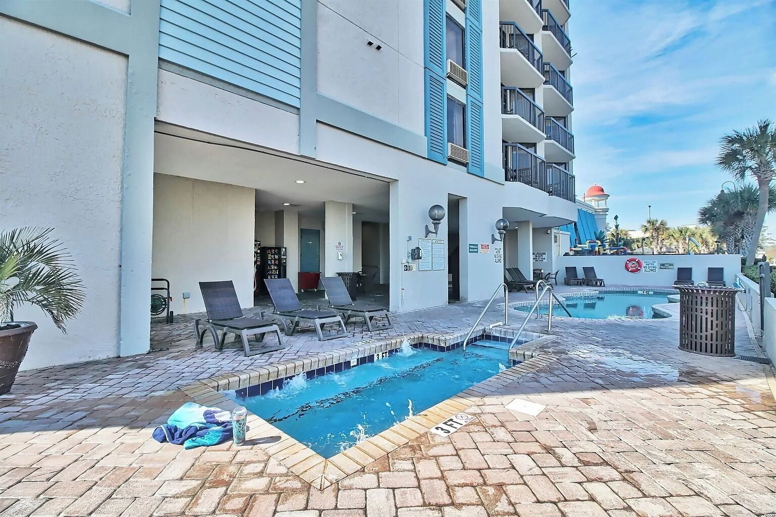 A pool area with lounge chairs, a small pool, and a building with balconies.