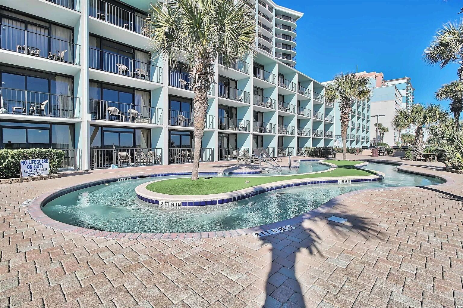 A hotel with a pool area, palm trees, and a sign indicating no lifeguard on duty.