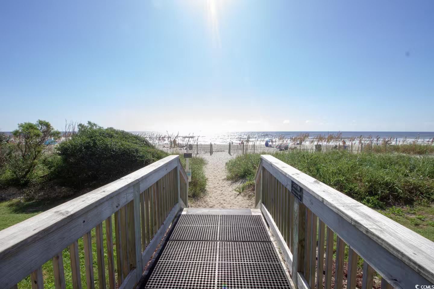 Ein hölzerner Steg führt zu einem Strand unter blauem Himmel.