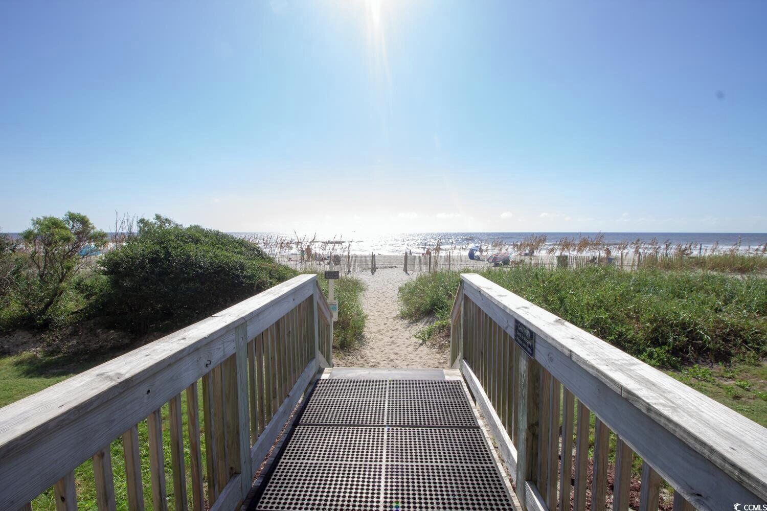 A wooden boardwalk leading to a beach with a clear view of the ocean.