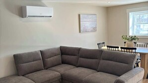Ein modernes Wohnzimmer mit einem Ecksofa, einem runden Couchtisch und einem Essbereich mit Tisch und Stühlen.