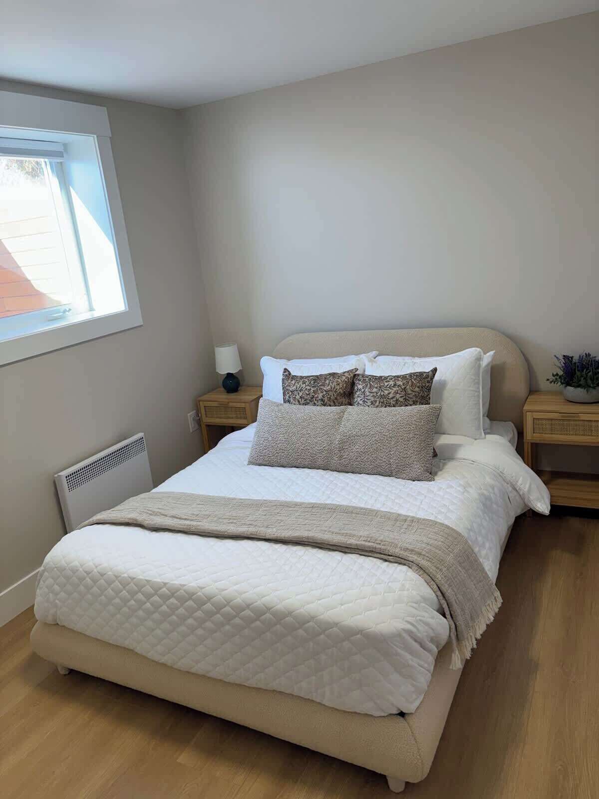A neatly made bed with a quilted duvet, a bedside lamp, and a small potted plant on the nightstand.