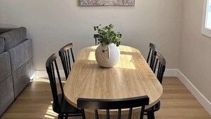Ein Essbereich mit Holztisch, schwarzen Stühlen, einer weißen Vase mit Grünpflanzen und einem Bild an der Wand.