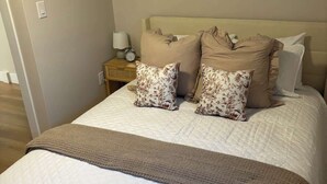 Ein ordentlich bezogenes Bett mit einer gesteppten weißen Daunendecke, zwei Kissen mit Blumenmuster und einer braunen Tagesdecke.
