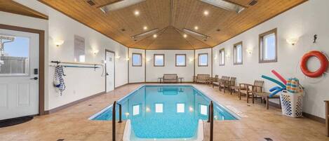 Une piscine intérieure avec un plafond en bois, un sol carrelé et plusieurs fenêtres.