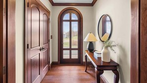 A hallway with wooden doors, a mirror, a lamp, and a vase with flowers. - New Glasgow Pool House - Indoor Pool - Sleeps 14 (New Glasgow)