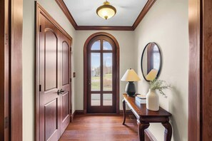 A hallway with wooden doors, a mirror, a lamp, and a vase with flowers. - New Glasgow Pool House - Indoor Pool - Sleeps 14 (New Glasgow)