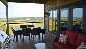 A covered outdoor area with a table and chairs, a grill, and a sofa with a patterned cushion. - New Glasgow Pool House - Indoor Pool - Sleeps 14 (New Glasgow)
