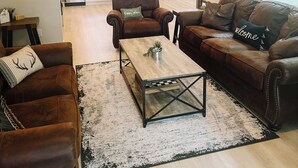 Sala de estar con sofá, sillón y mesa de centro, una cocina al fondo y un comedor.