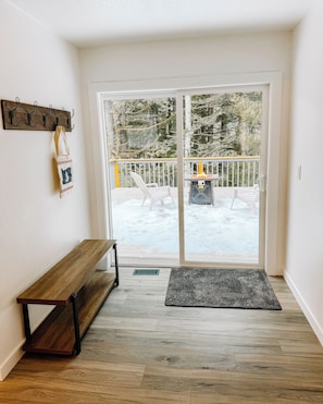 A room with a bench, a coat rack, and a view of a snowy deck outside.