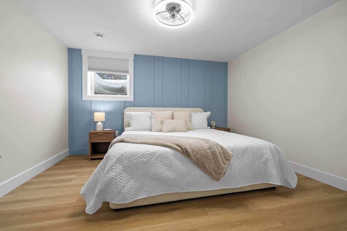 Une chambre à coucher comprenant un lit, une table de chevet, une lampe, une fenêtre avec des stores et un ventilateur de plafond.