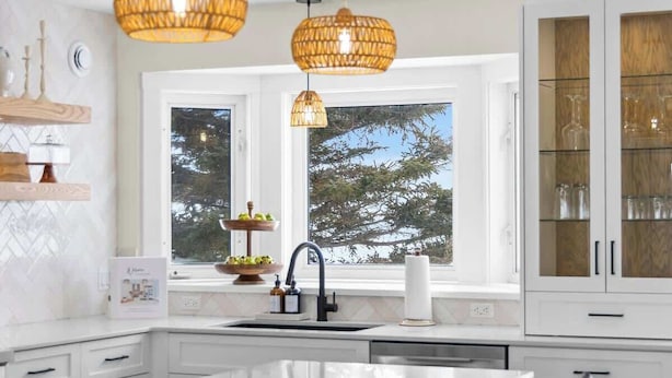 A modern kitchen with a large island, pendant lights, and a view of trees outside.