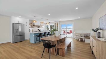 Een moderne keuken met een centraal eiland, een eethoek met een houten tafel en stoelen, en uitzicht op de omgeving.