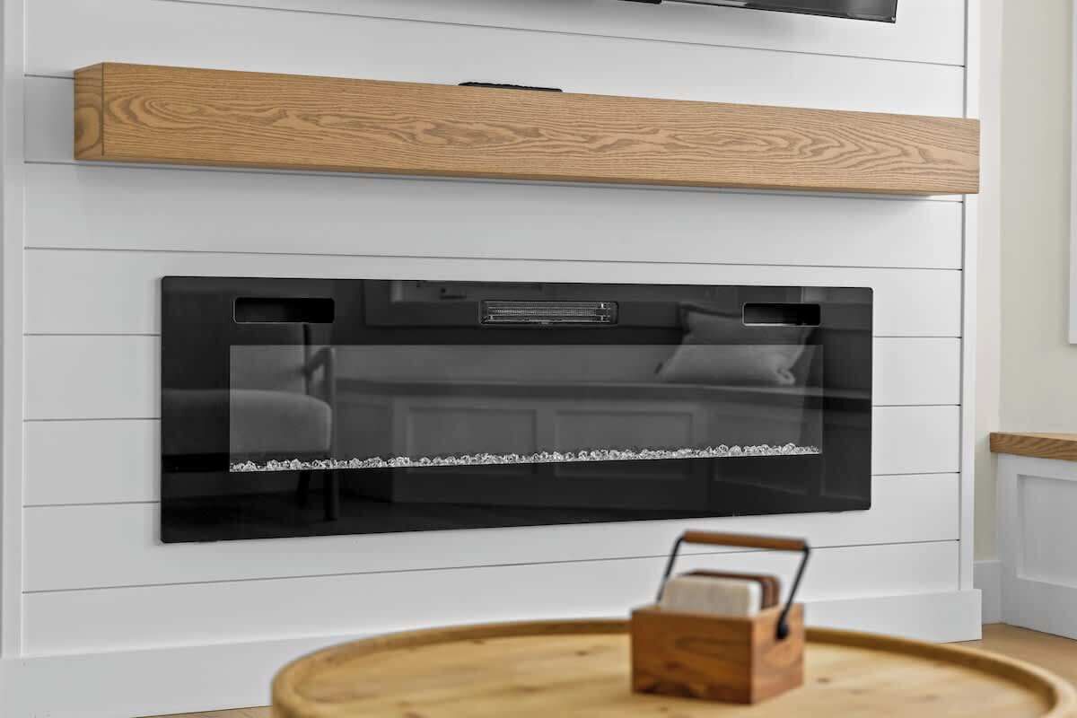 A modern kitchen with a built-in black oven, white wall paneling, and a wooden shelf above.