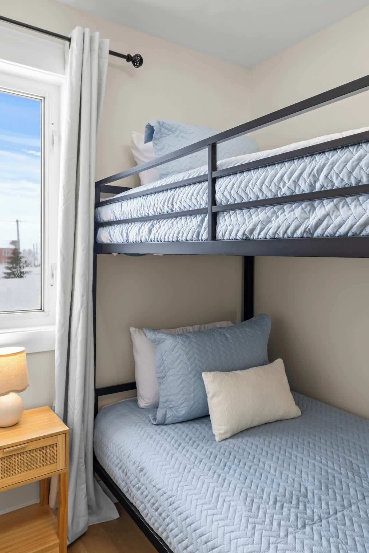 A bunk bed with a headboard, a bedside table with a lamp, and a window with curtains.