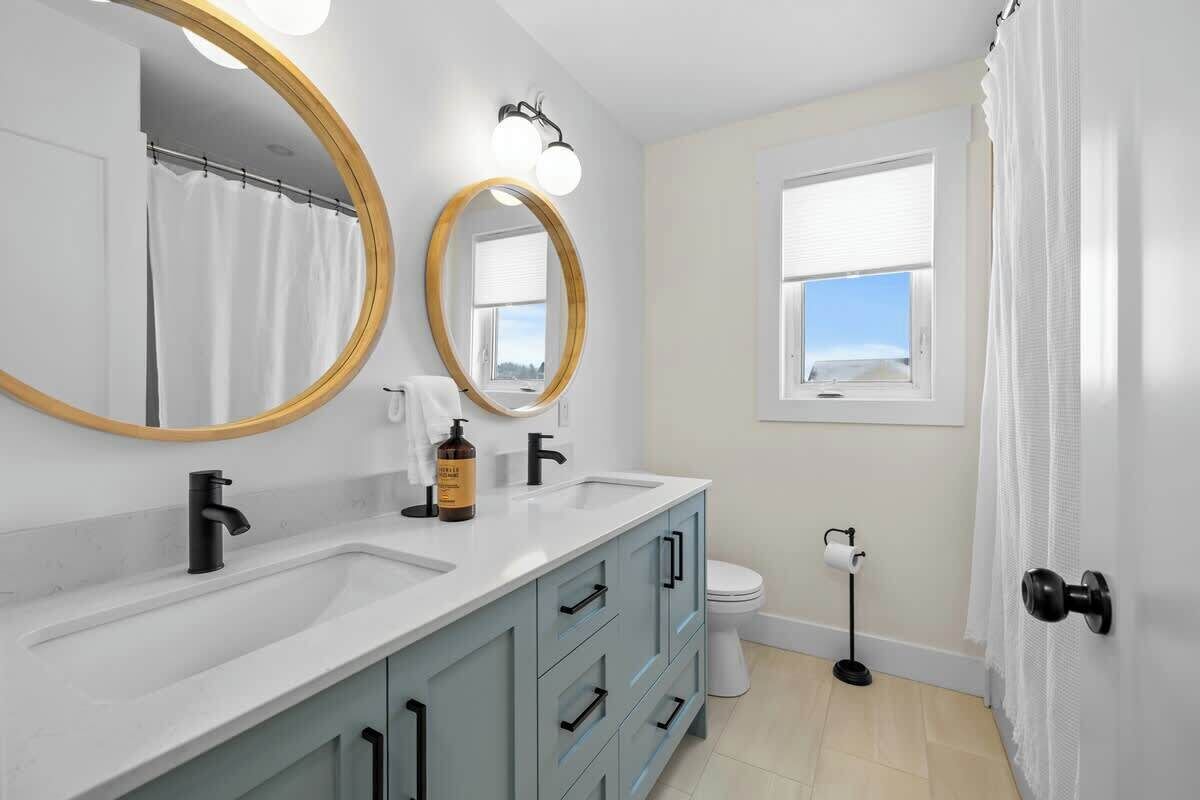 A bathroom with two sinks, a toilet, a window, and a mirror with a wooden frame.