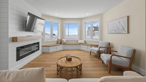 A modern living room with a fireplace, a television mounted on the wall, a round wooden coffee table, and seating arrangements.